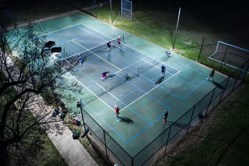 Aerial view of pickleball court with players illuminated for nighttime play